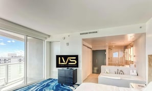 A modern hotel room with a large window, a flat-screen TV, a sofa, and a bathroom with a large mirror. - LVS W FTL 1409 - Beachfront Resort Condo | 2 Bed / 2 Bath with Southeast Ocean View (Fort Lauderdale)