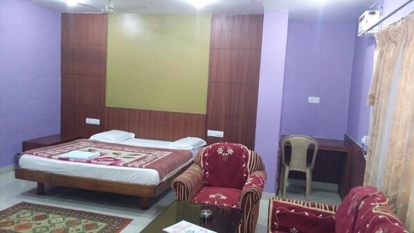 A hotel room with a bed, a red armchair, a small desk, and a chair.