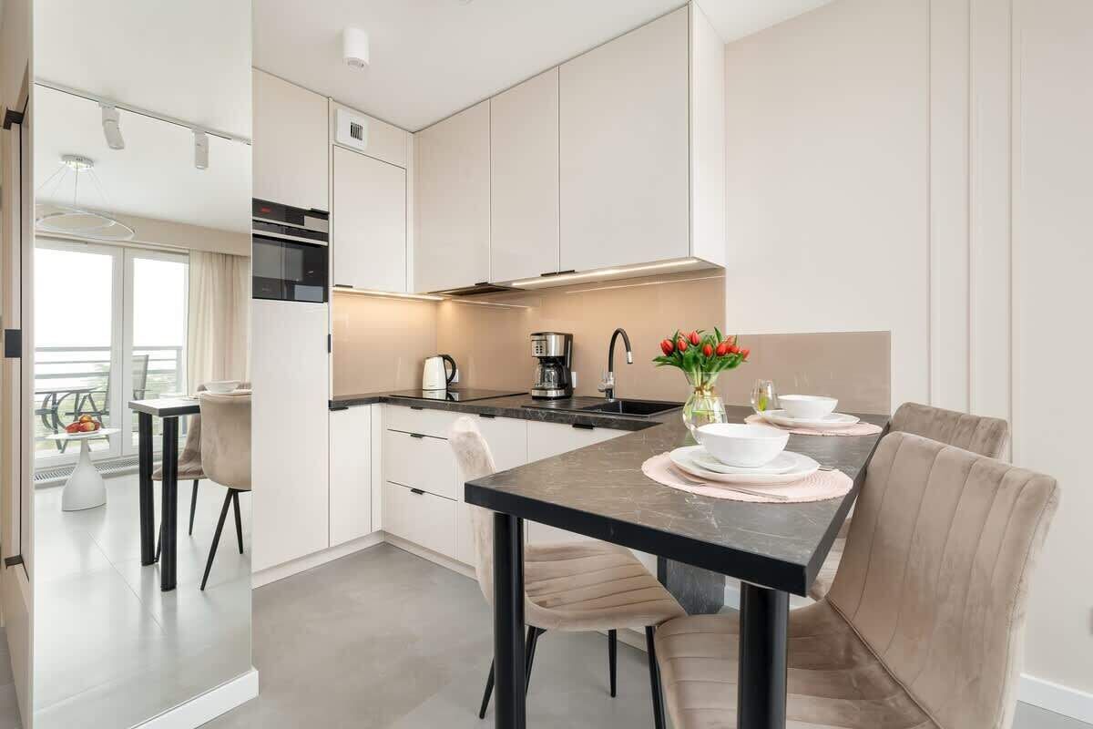 Una cocina moderna con una isla central, armarios blancos y una zona de comedor con una mesa dispuesta para cuatro.