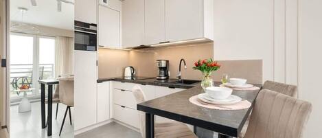 Una cocina moderna con una isla central, armarios blancos y una zona de comedor con una mesa dispuesta para cuatro.