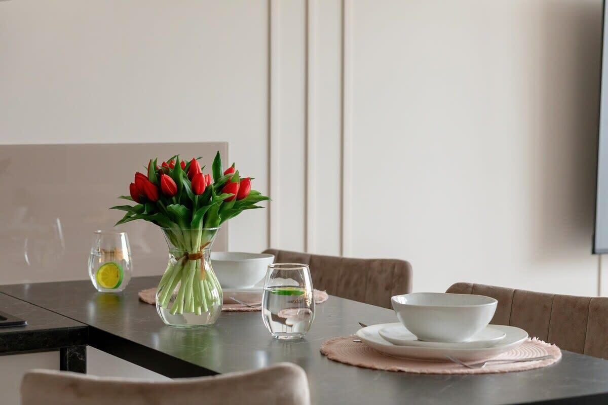 A dining table set with a vase of red tulips, a glass of water, and a bowl on a placemat.