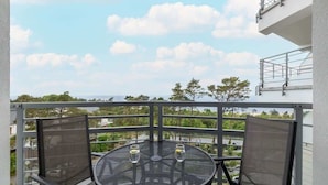 A balcony with a round table and two chairs, overlooking a residential area with trees and houses.