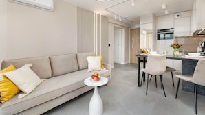 A modern living room with a sofa, a dining table, and a kitchen area.