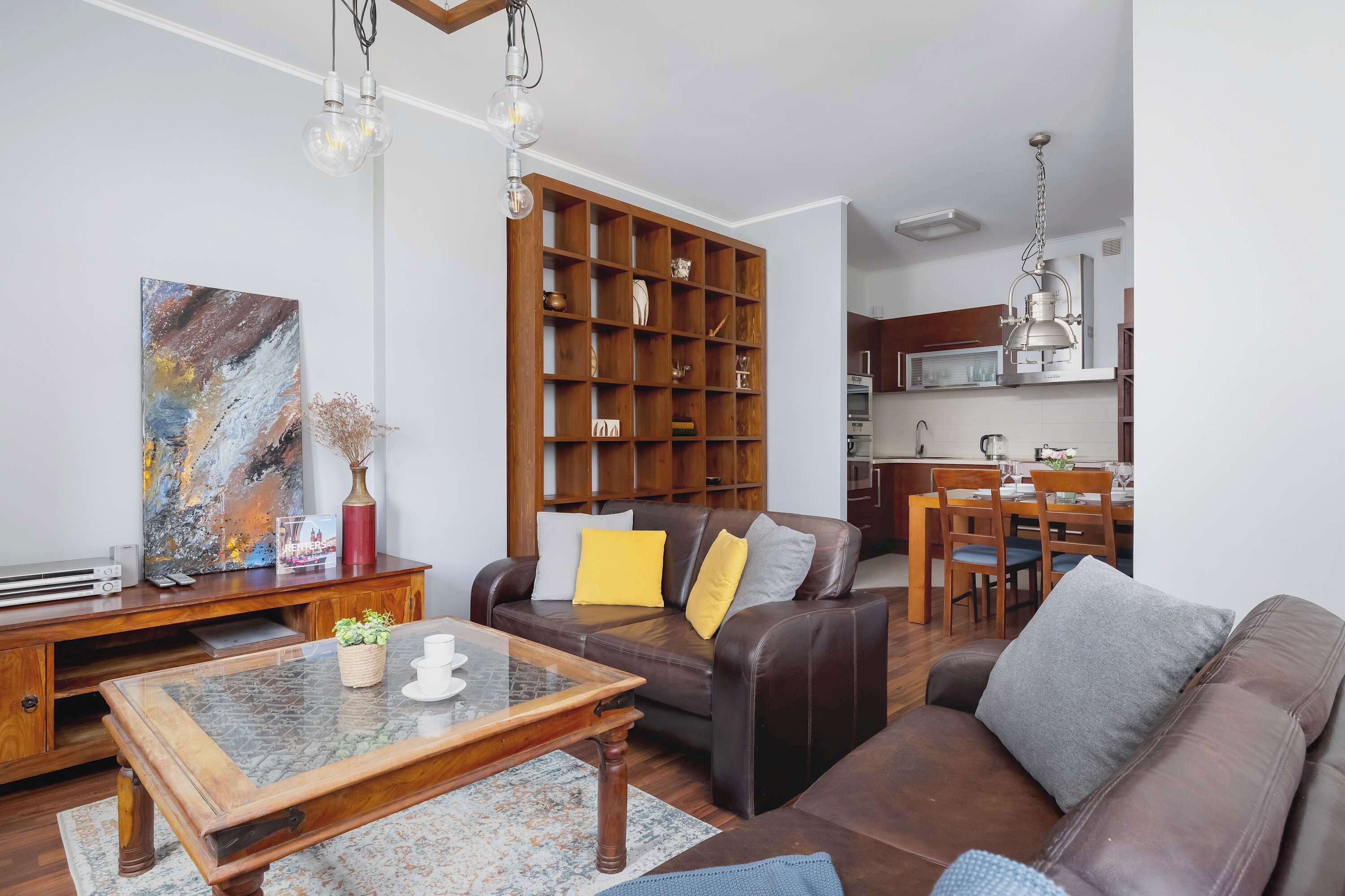 A living room with a brown leather sofa, a wooden coffee table, and a bookshelf.