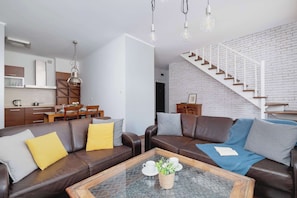 Een moderne woonkamer met leren banken, een glazen salontafel en een trap met witte leuningen.