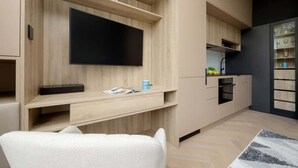 A modern kitchen with built-in appliances, a flat-screen TV, and a dining area with a white chair. - Stylish Studio in the Heart of Warsaw | Close to Lazienki Krolewskie Park (Warszawa)