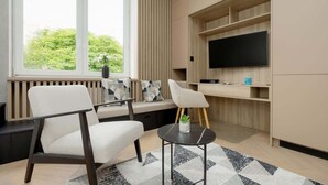 A modern living room with a sofa, chairs, a coffee table, and a TV mounted on a wooden wall. - Stylish Studio in the Heart of Warsaw | Close to Lazienki Krolewskie Park (Warszawa)
