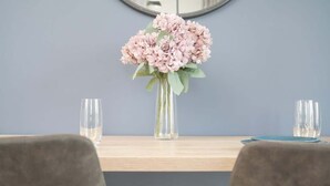 Una mesa con un florero, dos vasos y un mantel individual azul.