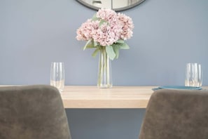 A table with a vase of flowers, two glasses, and a blue placemat.