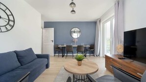 Una sala de estar moderna con un sofá, una mesa de centro, un televisor y una zona de comedor con sillas y una mesa.