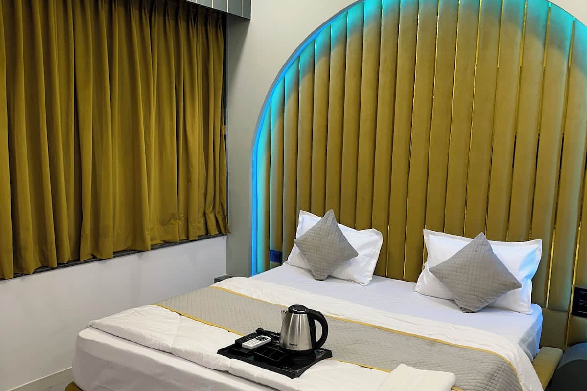 Una habitación de hotel moderna con una cama grande, una mesita de noche con hervidor y un original cabecero curvo.