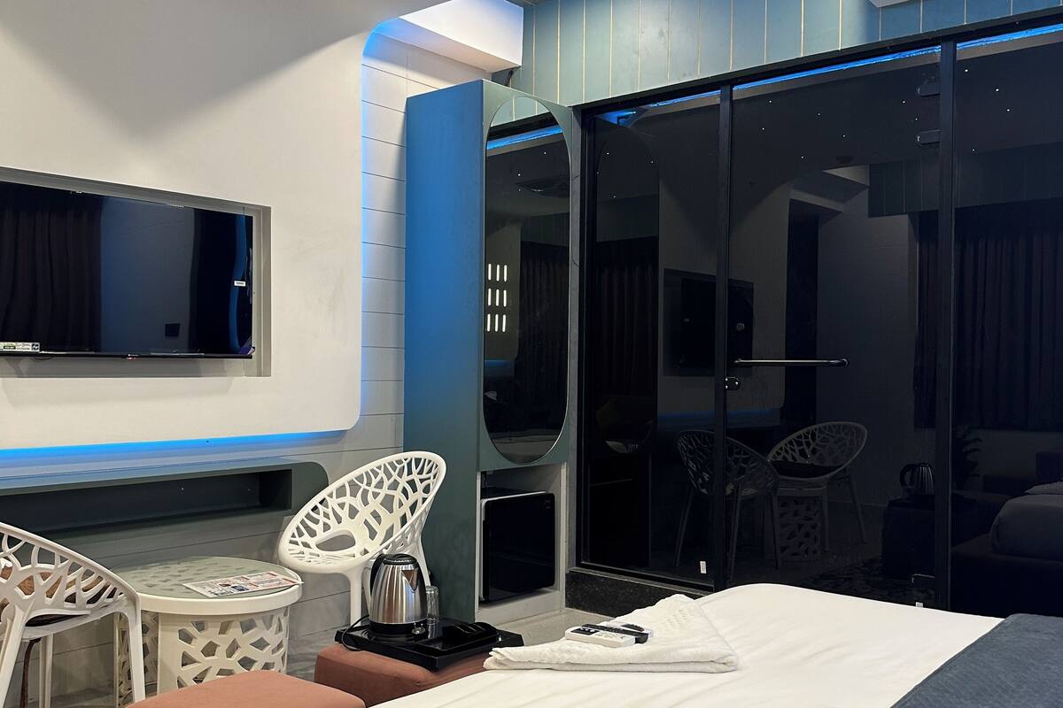 Habitación de hotel moderna con cama, televisor de pantalla plana, zona de estar con sillas y puerta de cristal corredera que da a un balcón.