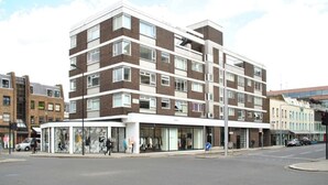 Un immeuble à plusieurs étages doté d’une architecture moderne, caractérisé par un mélange de briques et de façades blanches, de grandes fenêtres et un espace commercial situé au rez-de-chaussée.