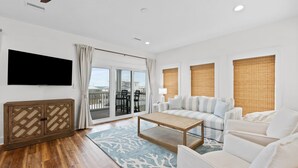 A spacious living room with a large TV, a sofa, a coffee table, and a view of the outdoors through a sliding glass door. - Twist of Lime - Mexico Beach, Unobstructed Gulf view, Elevator, Private Pool, Tw (Mexico Beach)