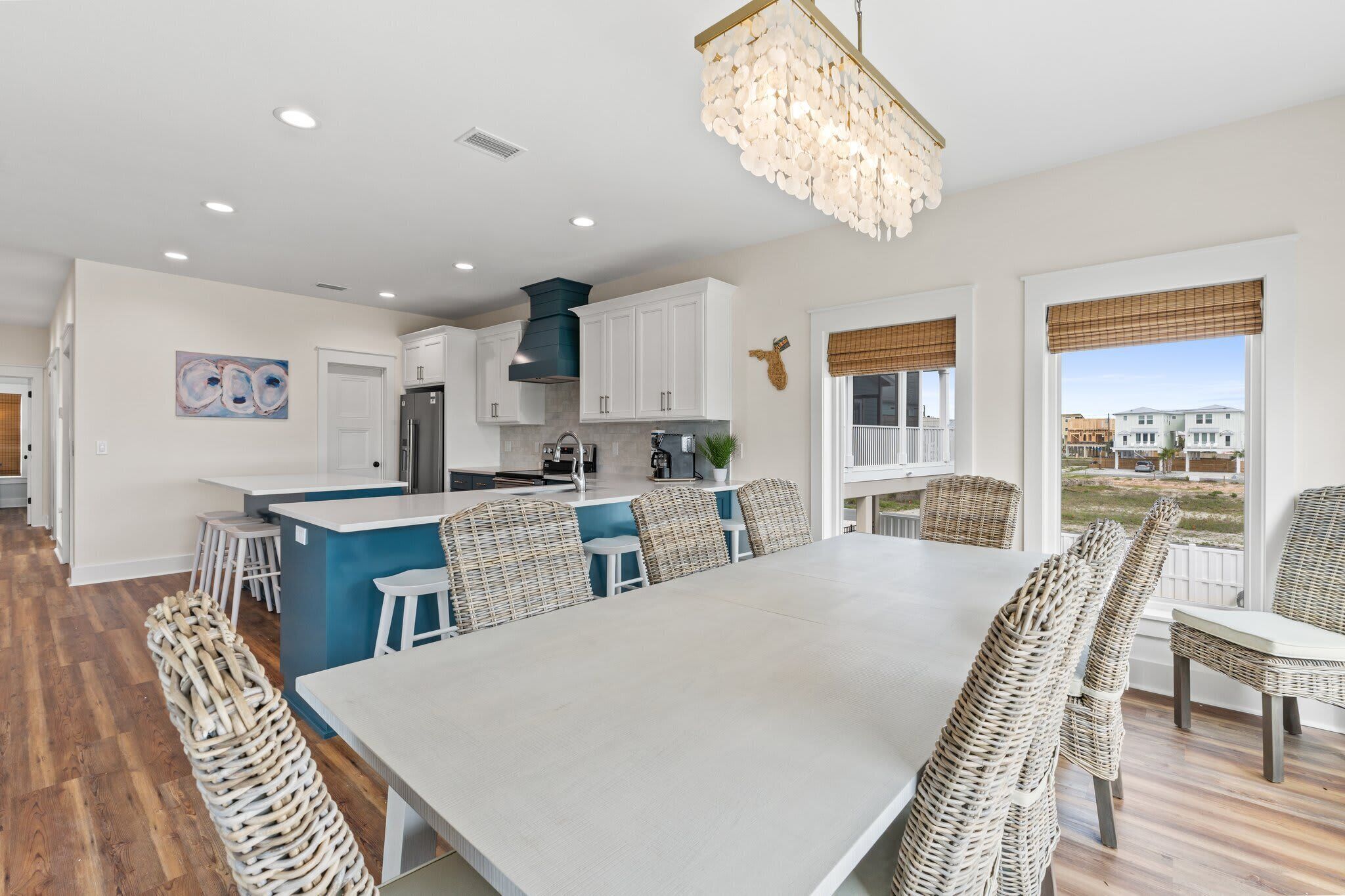 A modern kitchen with white cabinets, a central island, and a dining area with wicker chairs.