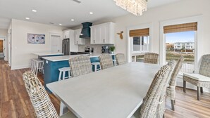 A modern kitchen with white cabinets, a central island, and a dining area with wicker chairs. - Twist of Lime - Mexico Beach, Unobstructed Gulf view, Elevator, Private Pool, Tw (Mexico Beach)