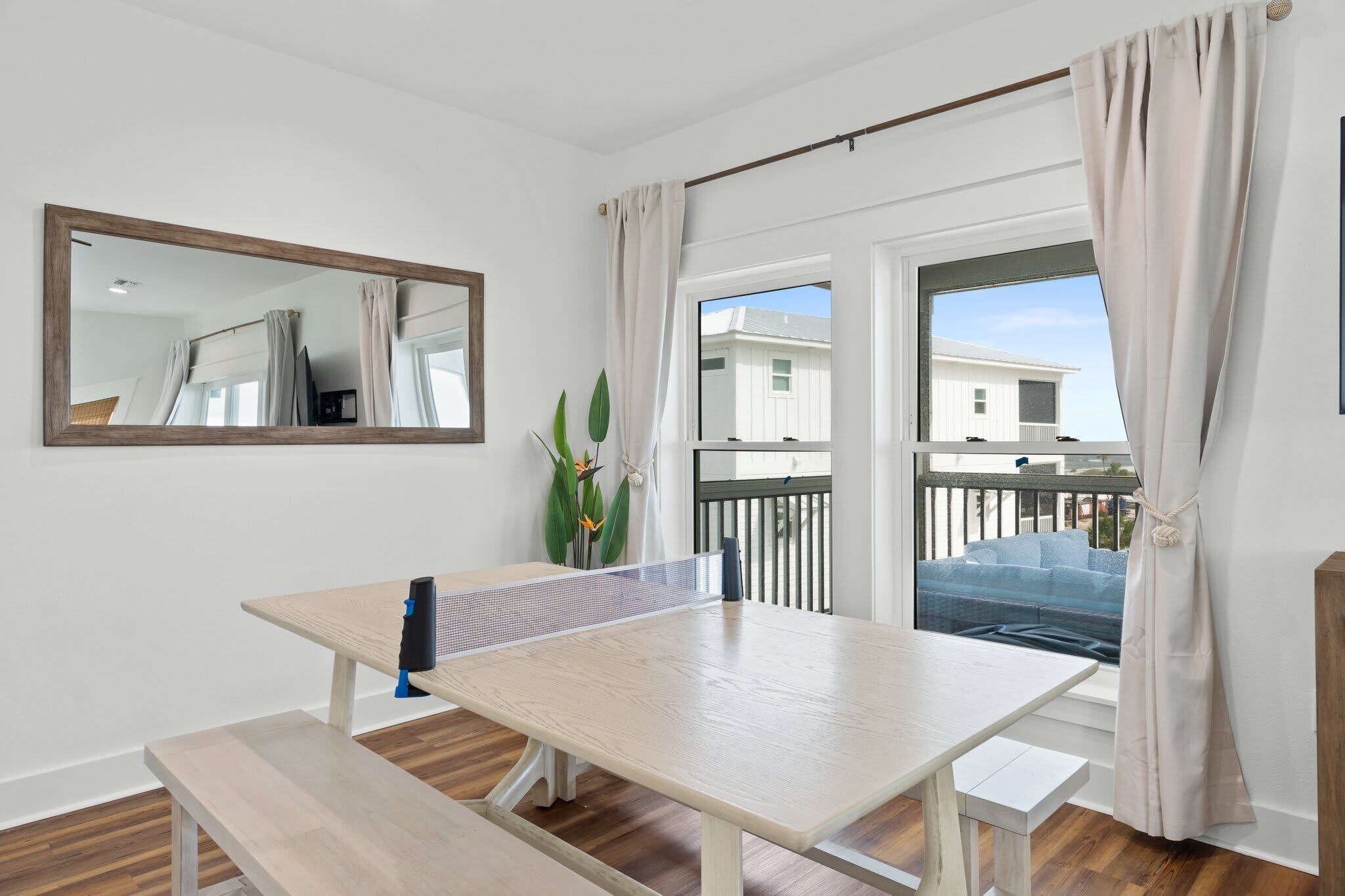 A room with a ping pong table, a bench, a mirror, and a view of a balcony with a railing.