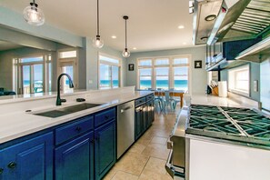 Una cocina moderna con una isla grande, electrodomésticos integrados y vista al océano.