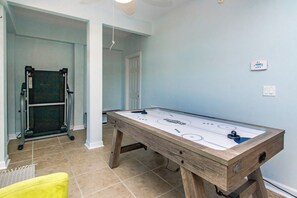 Una habitación con mesa de juego de trinquete, cinta de correr y puerta que da a otra habitación.