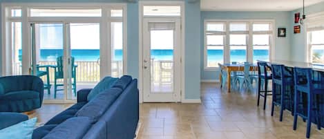 A spacious living area with a large sofa, a dining table with chairs, and a view of the ocean through large windows.