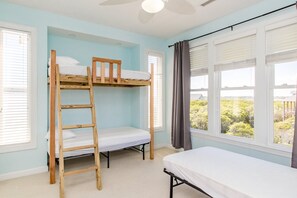Una habitación con literas, una escalera, cama individual y ventanas grandes con persianas.