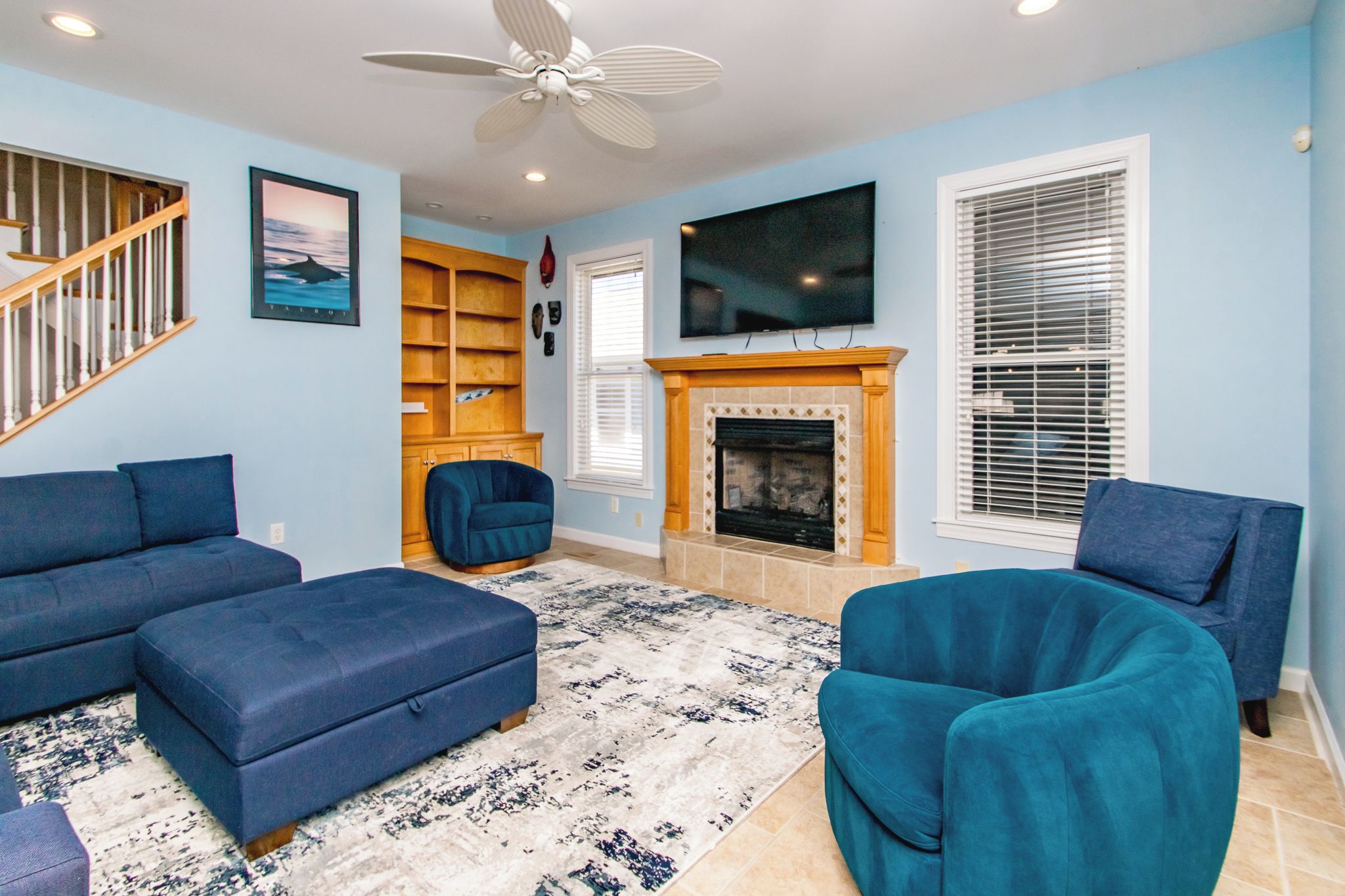 A living room with a fireplace, blue sofas, a ceiling fan, and a TV mounted on the wall.