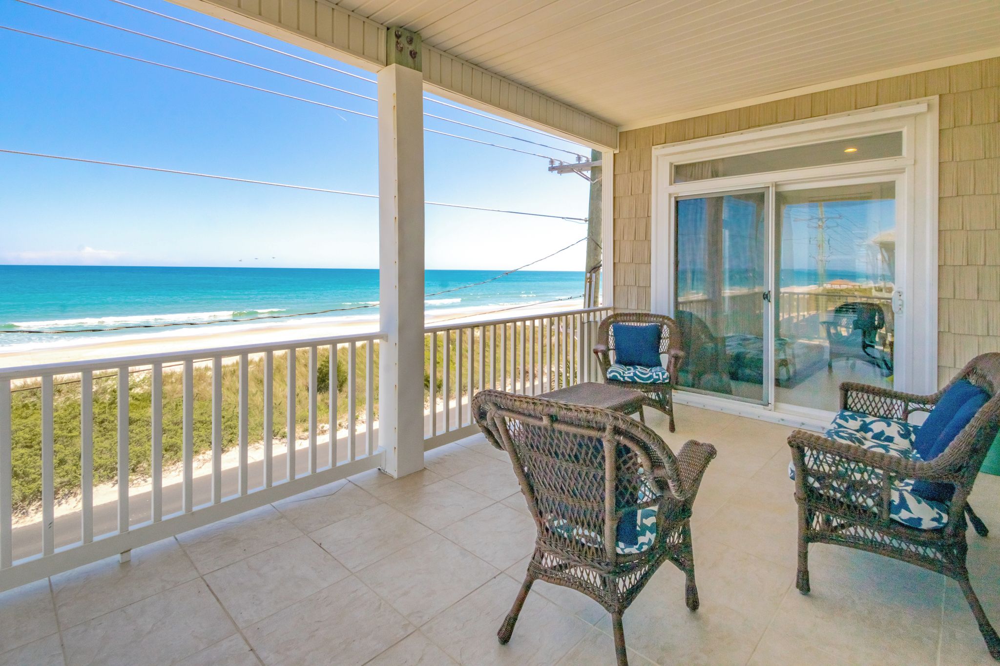 A covered balcony with wicker furniture and a view of the beach.