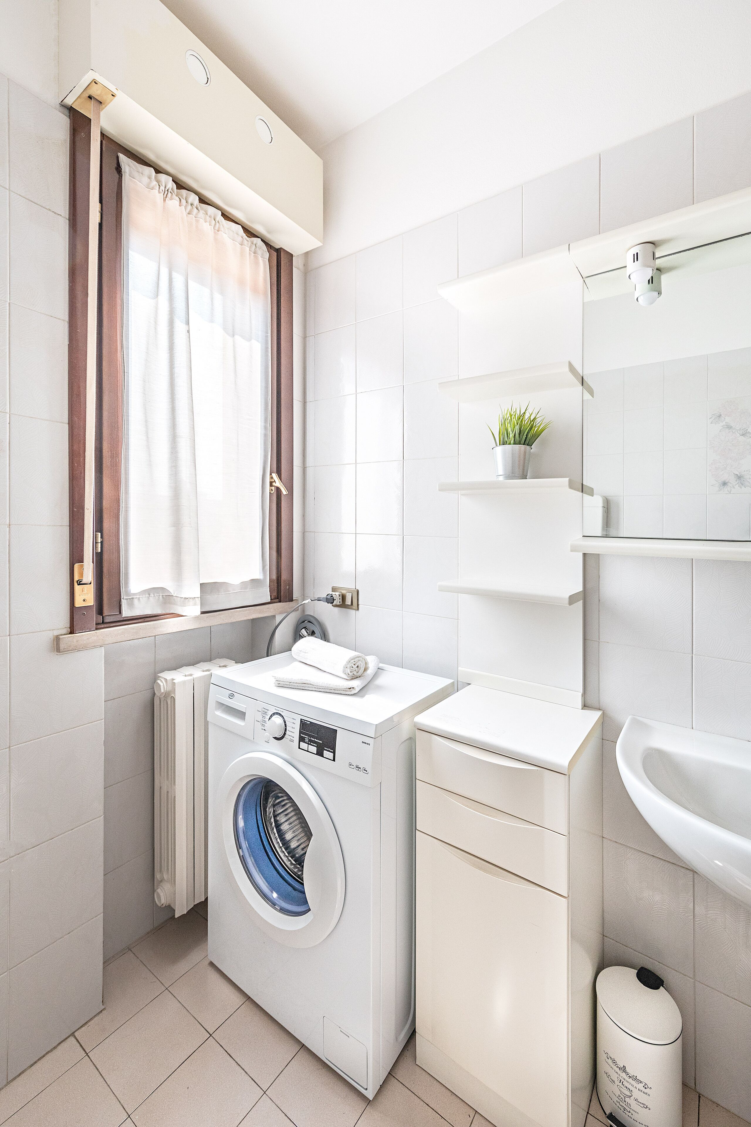 Ein kleines, modernes Badezimmer mit Waschmaschine, Waschbecken und einem Regal mit einer Pflanze.