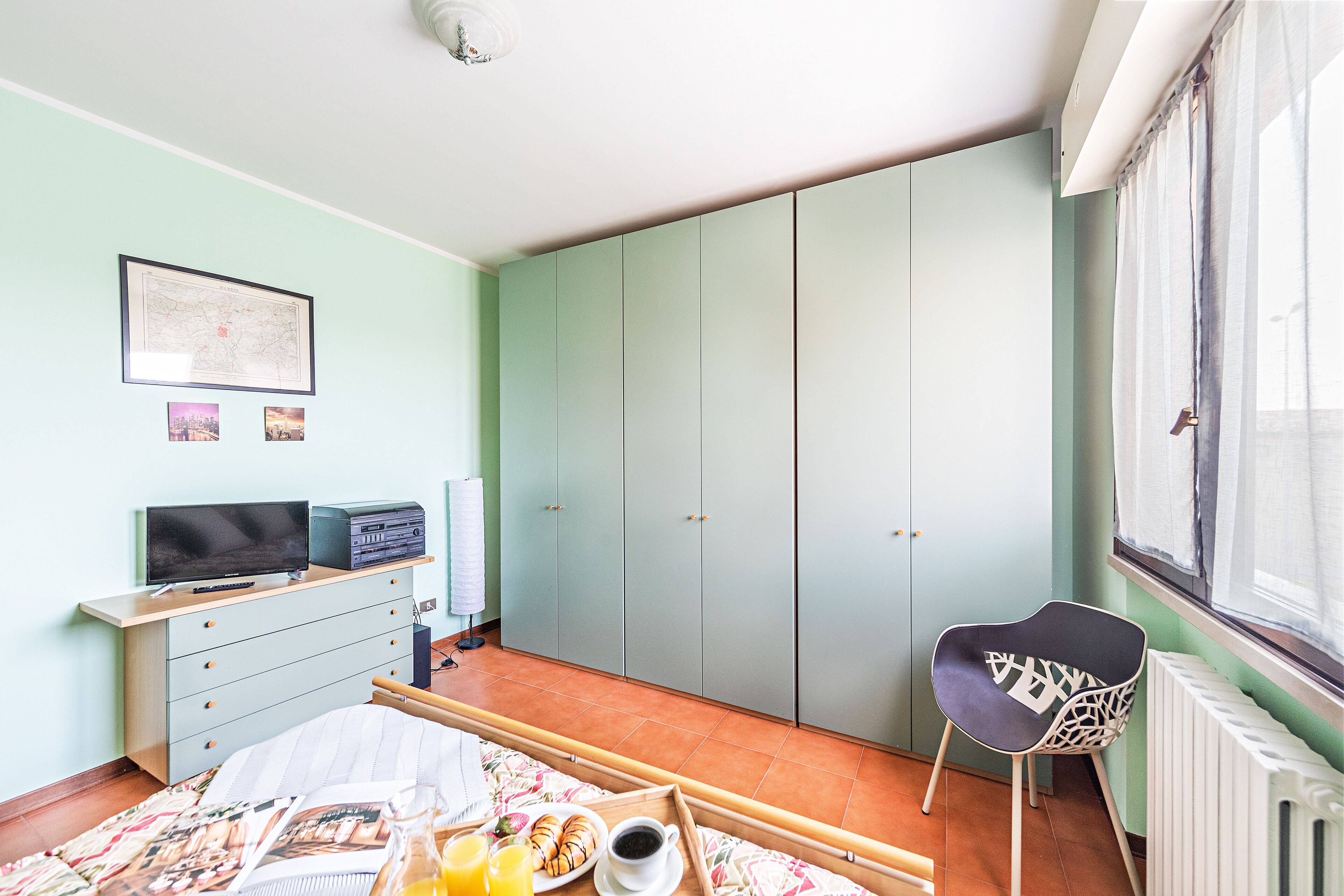 Quarto com cama, cómoda, cadeira, janela e radiador.