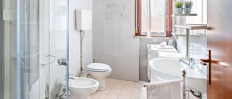 A modern bathroom with a glass shower enclosure, a toilet, a sink, and a window with curtains.
