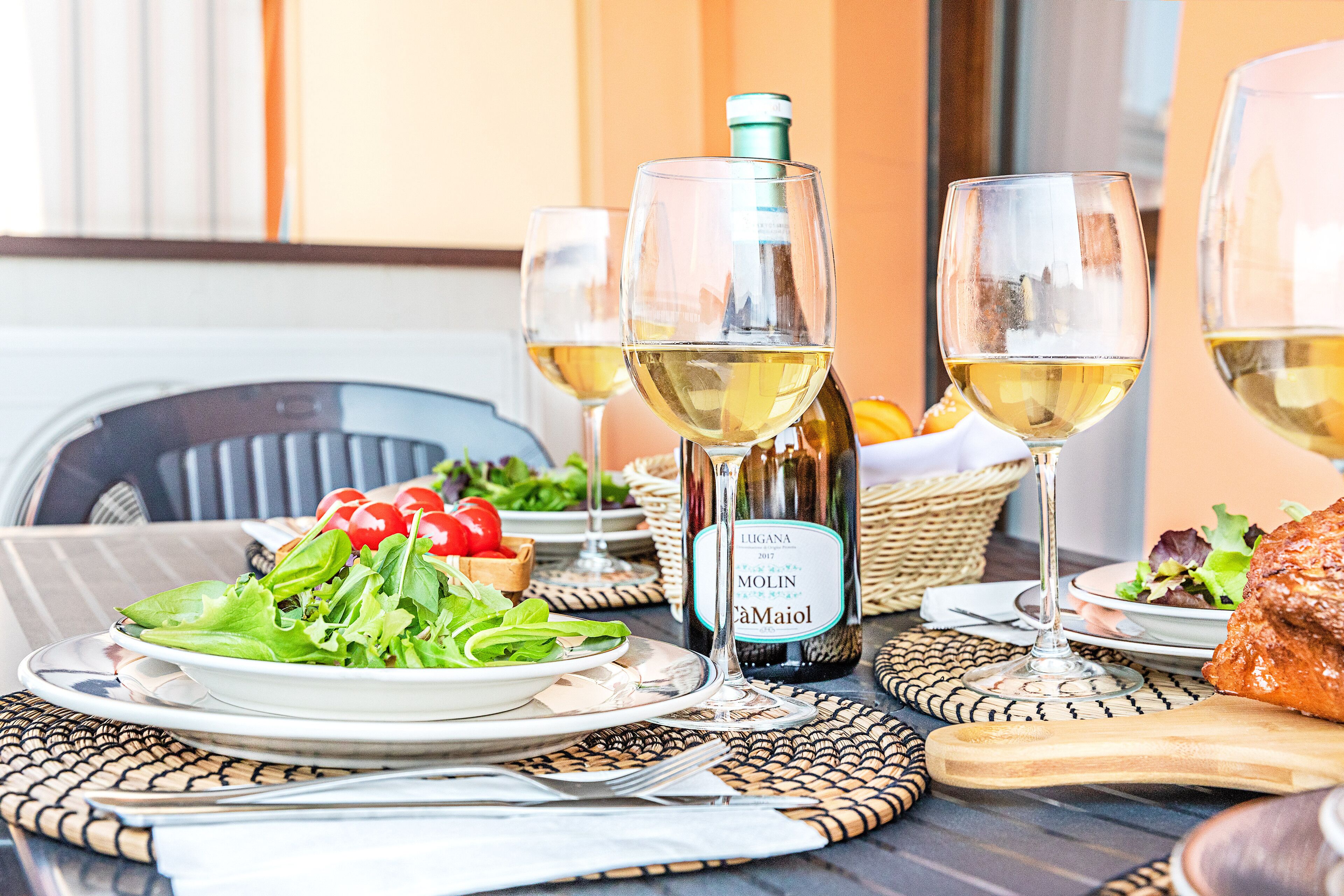 Una mesa servida con una botella de vino, dos copas, un plato de ensalada y una tabla de madera.