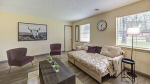 A bedroom with a bed, two chairs, a coffee table with plants, a clock, and a window with blinds. - Indoor fireplace with patio and pool table (Beaumont)