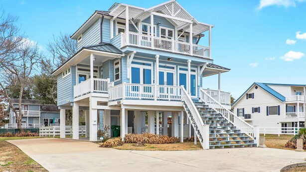 Ein zweistöckiges Strandhaus mit Balkon, überdachter Veranda und Treppe zum Obergeschoss.
