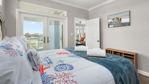 Ein Schlafzimmer mit Bett, Deckenventilator, einem Gemälde und Blick durch eine Glastür.