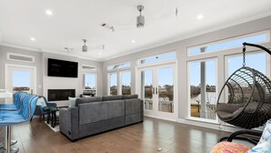 Ein geräumiges Wohnzimmer mit grauem Sofa, blauem Sessel, Hängesessel und einem an der Wand befestigten Fernseher.