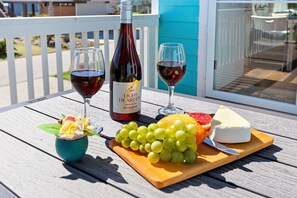 A wooden table with a bottle of wine, two glasses of red wine, a wooden board with grapes, a cheese, and a small vase with flowers. - Welcome to Blue Jewel! (Galveston)