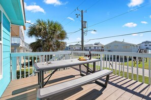 A wooden deck with a picnic table and benches, overlooking a residential area with houses and a palm tree. - Welcome to Blue Jewel! (Galveston)