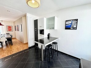Una cocina moderna con encimera negra, armarios blancos y un comedor con mesa y sillas de madera.
