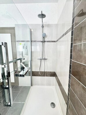 Un baño moderno con cabina de ducha de vidrio, un estante de vidrio y una pared revestida con mosaicos y una franja decorativa.