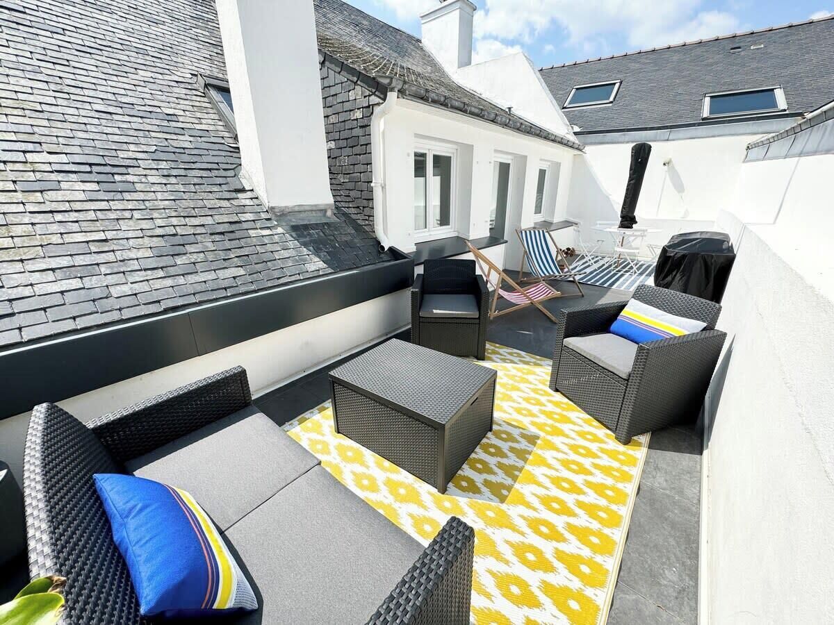 An outdoor seating area with wicker furniture, a patterned rug, and a view of a building with a sloped roof.
