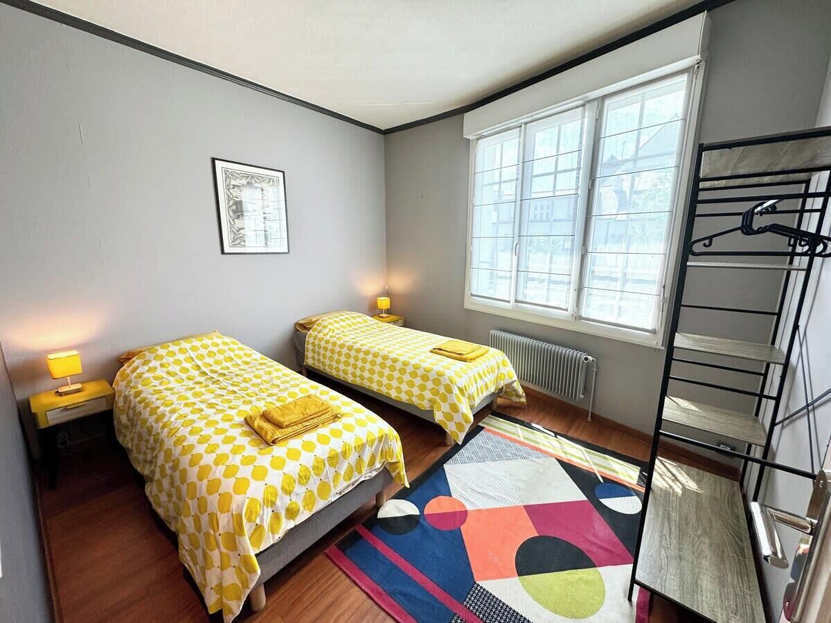 Une chambre avec deux lits simples, un radiateur, une fenêtre et un lit superposé.