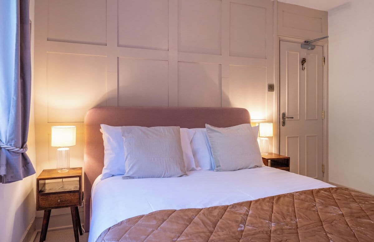 A neatly made bed with a pink headboard, two bedside lamps, and a wooden nightstand.