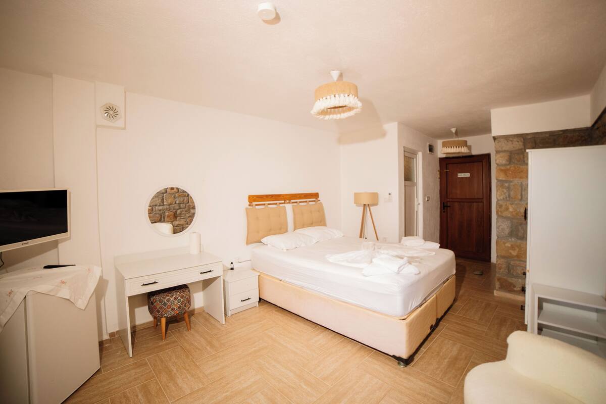 A bedroom with a bed, a desk, a chair, a TV, and a lamp.