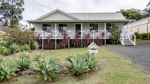 A two-story house with a covered porch, surrounded by a well-maintained garden with various plants. - Sandy Cottage in Narrawallee (Narrawallee)
