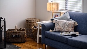 A modern living room with a blue sofa, a patterned pillow, a wicker basket, and a lamp. - Sandy Cottage in Narrawallee (Narrawallee)