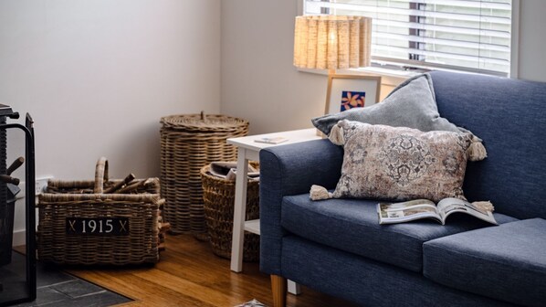 A modern living room with a blue sofa, a patterned pillow, a wicker basket, and a lamp. - Sandy Cottage in Narrawallee (Narrawallee)