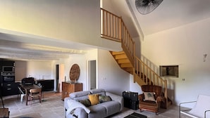 Ein geräumiger Wohnbereich mit hoher Decke, einer Treppe und einem Essbereich.