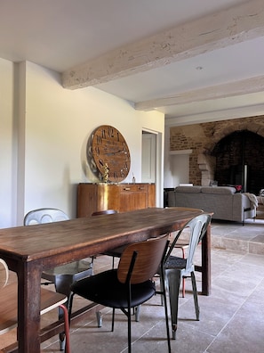 A dining area with a wooden table and chairs, a vintage clock, and a stone fireplace in the background. - La Métairie du Bézoué - Lannexe (Plumelec)