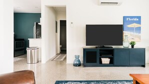 Un soggiorno moderno con una televisione a schermo piatto, un mobile TV blu scuro, un vaso blu e un poster a tema Florida.