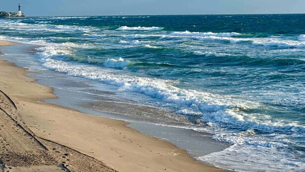 Una spiaggia con onde, un faro e cielo sereno.